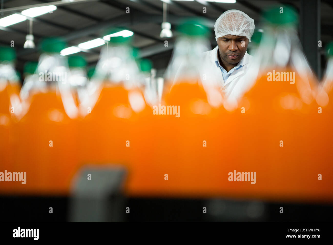 Serious male worker seen through orange juice bottles in factory Stock Photo