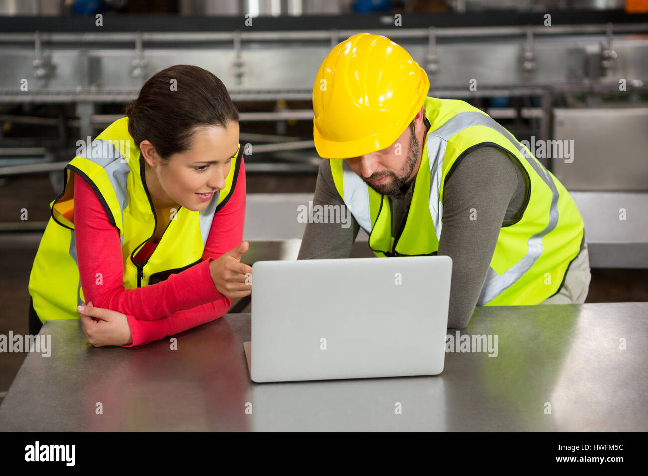 Male and female workers using laptop in factory Stock Photo