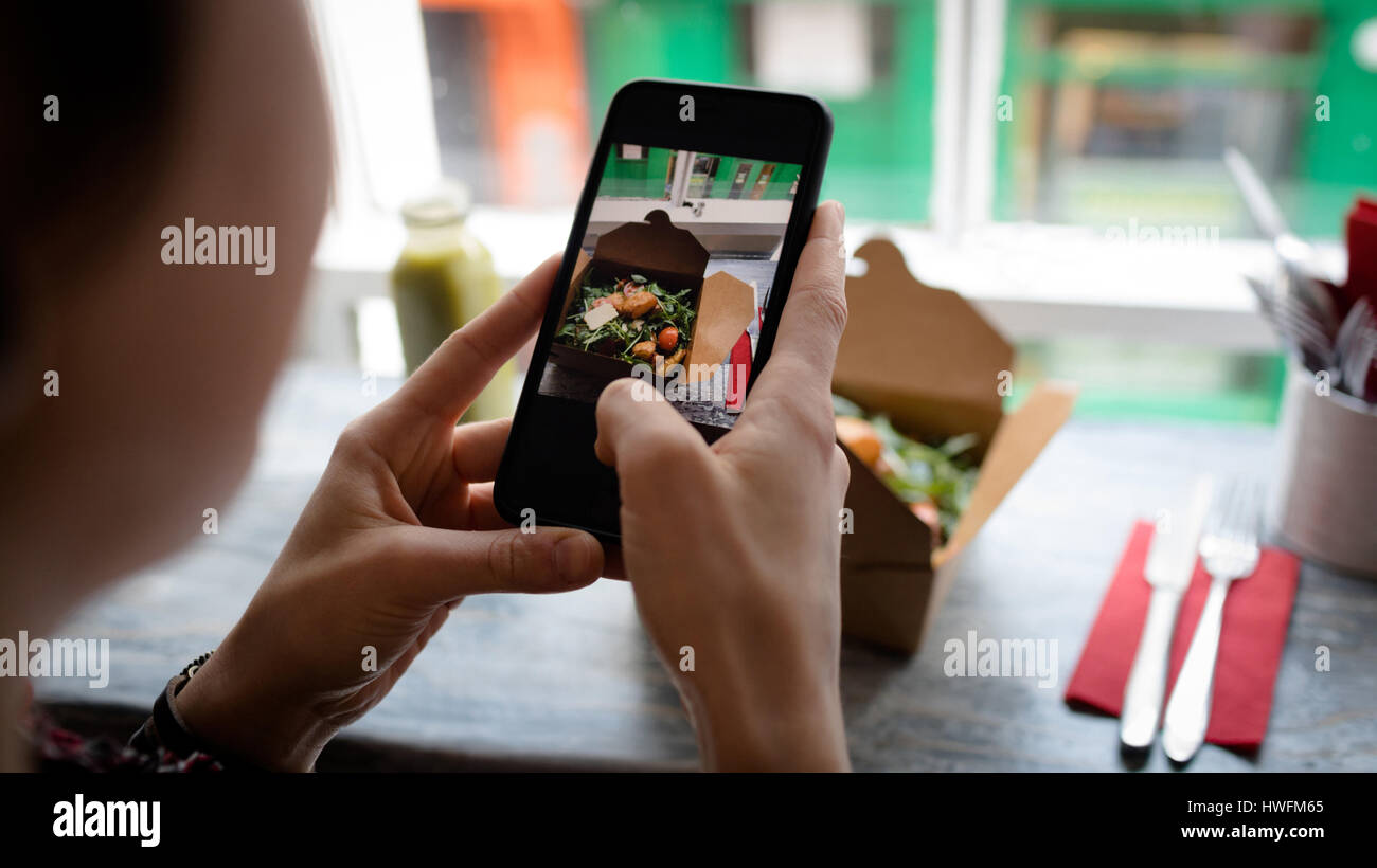 Woman clicking a photo of salad from mobile phone in cafÃƒÂ© Stock Photo