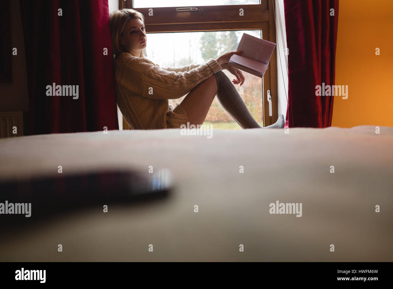 Woman sitting on window and reading a book at home Stock Photo - Alamy