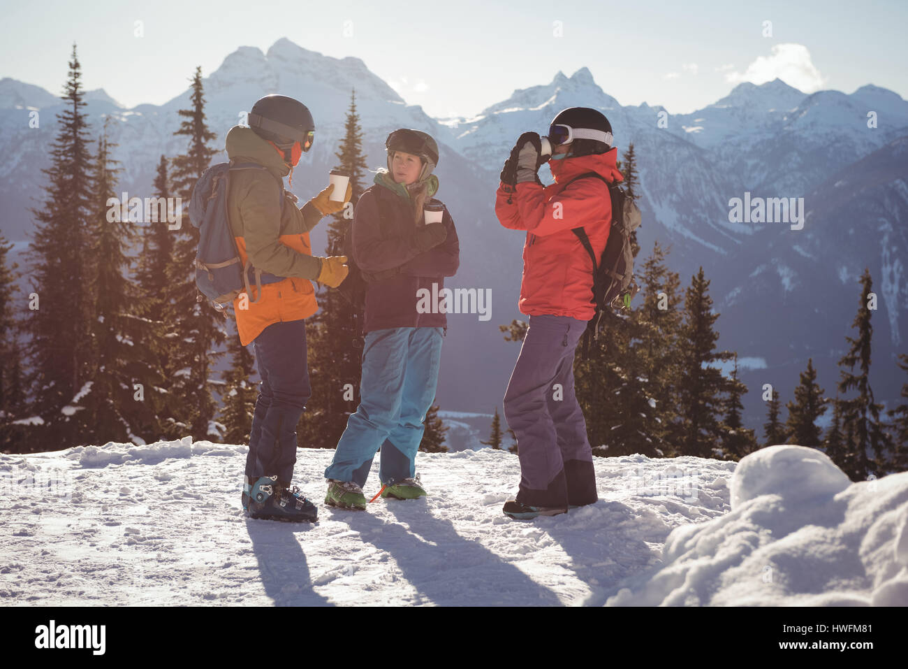 Skiers interacting with each other while having cup of coffee on snow covered mountain Stock Photo