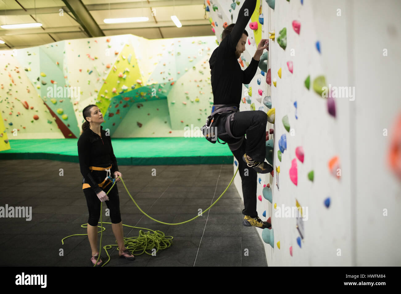 Trainer assisting man while climbing on artificial wall in gym Stock Photo