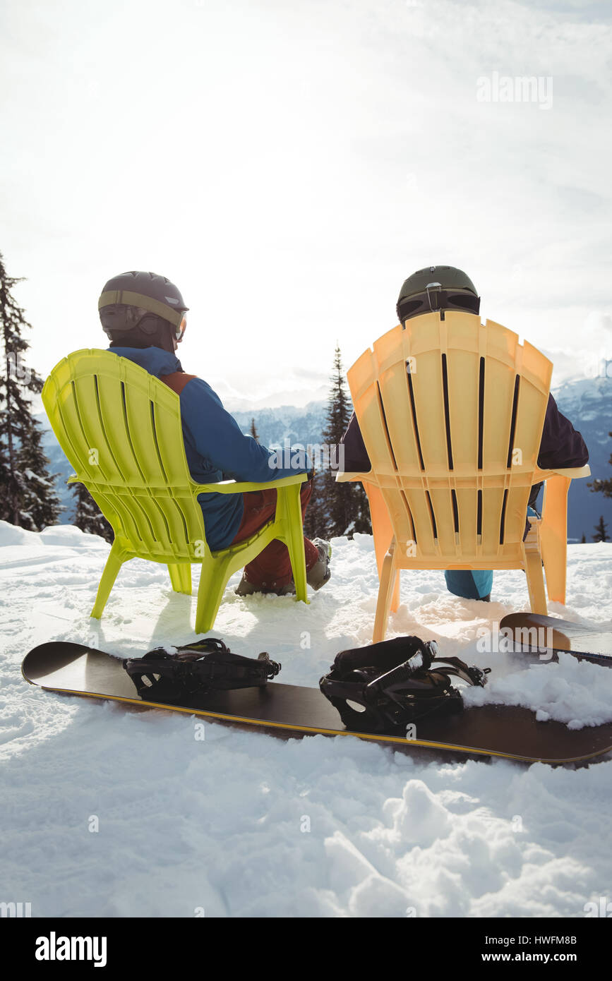 Rear view of couple sitting on mountain against sky during winter Stock Photo