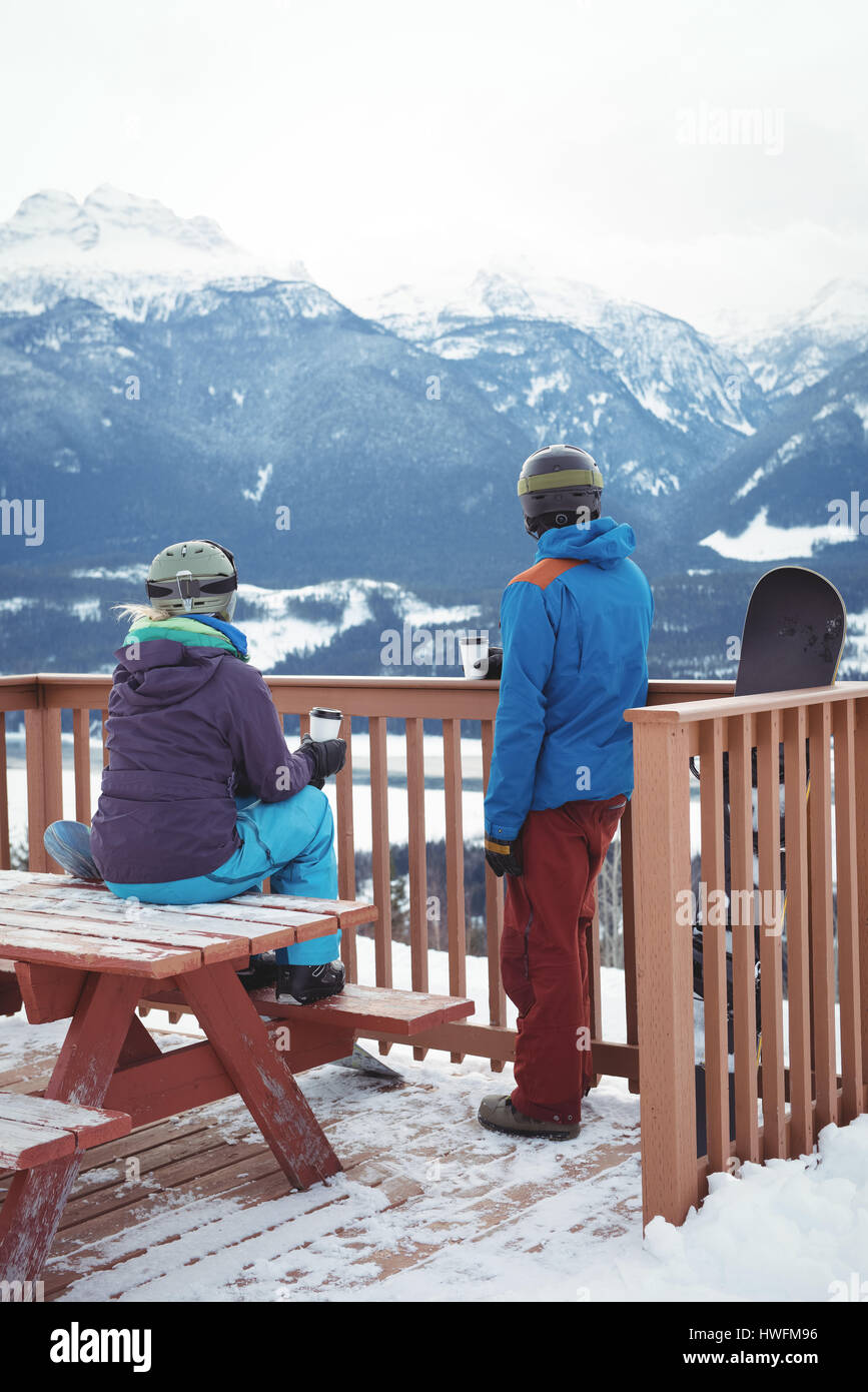 Rear view of couple by railing against snowcapped mountain during winter Stock Photo