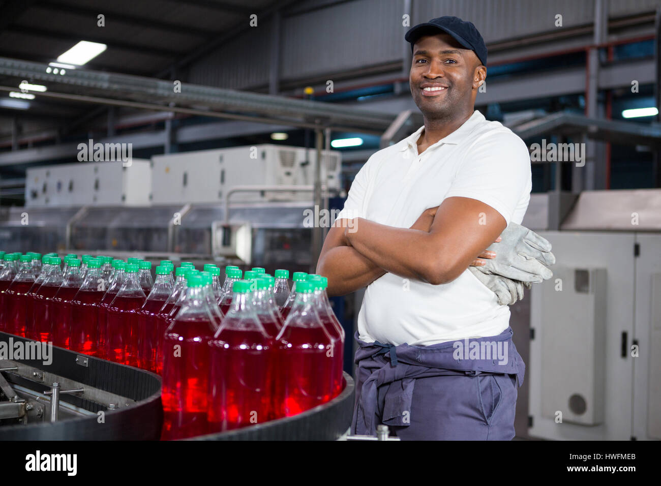 Portrait of male worker with arms crossed standing by bottles on production line in factory Stock Photo