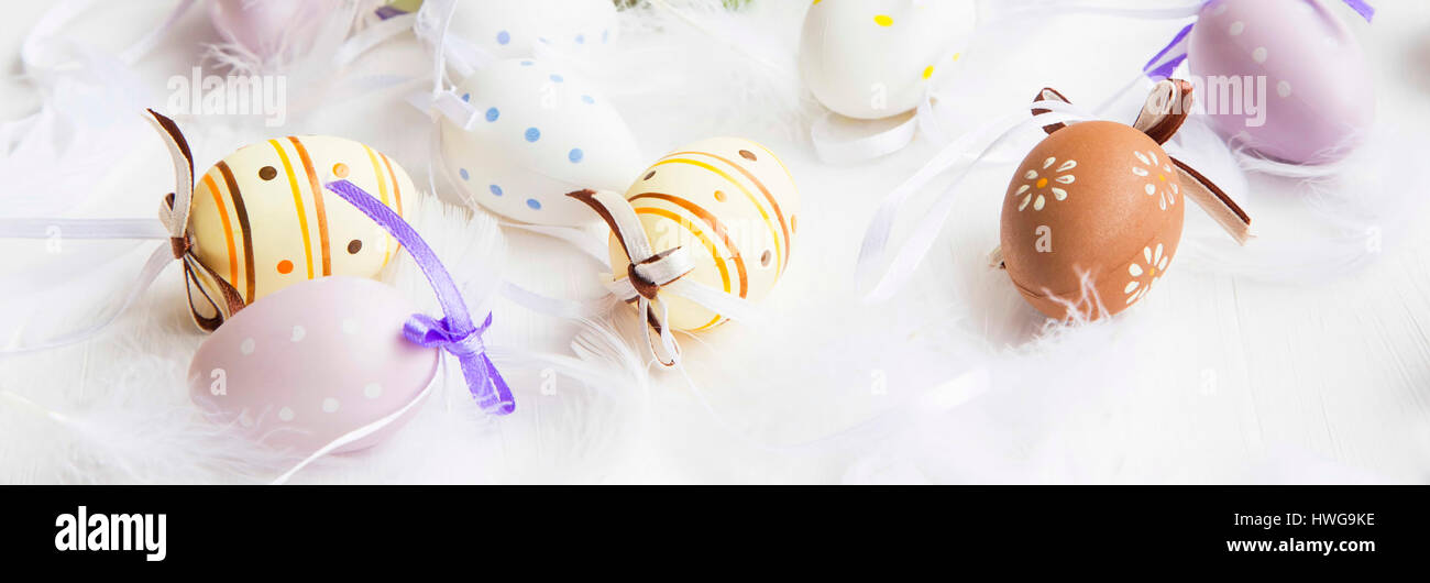 Easter eggs decorated with feathers on white painted wooden background ...