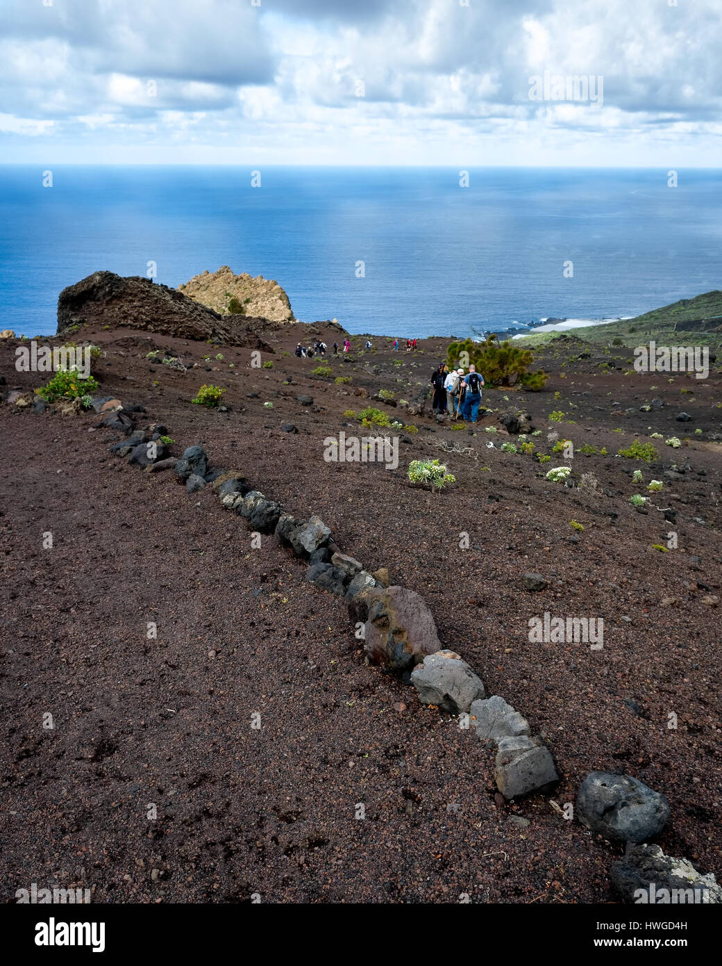 Cumbre Vieja, Fuencaliente. La Palma.  A distant view of the ancient rocks of the island that were buried in lava until recently rediscovered.  Hikers walking along the windy trail footpath that passes the ancient stone.  The footpath is marked out by a trail of lava rocks. Stock Photo