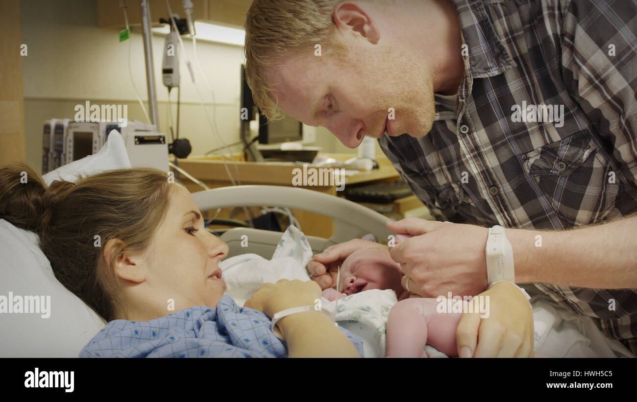 Profile view of new mother and father admiring newborn baby in hospital Stock Photo