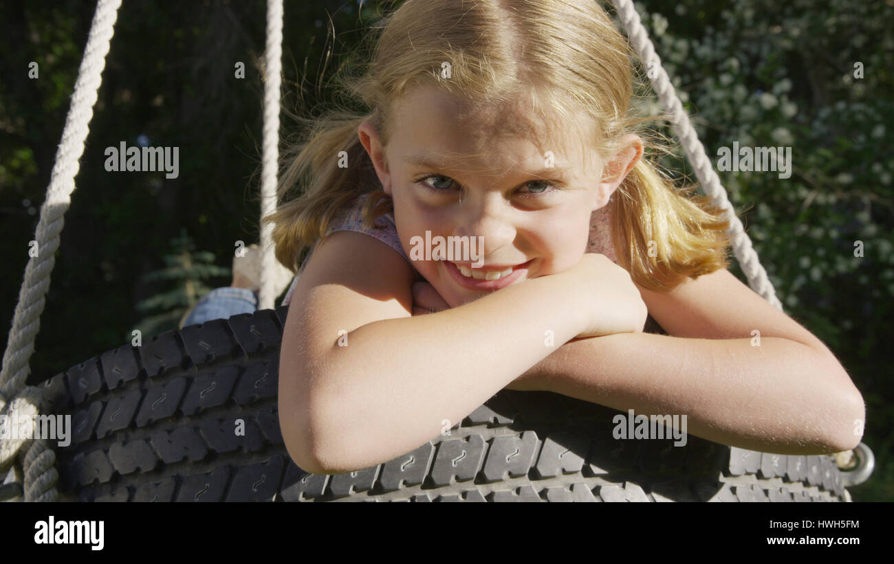 Close up portrait of smiling playful girl sitting on tire swing Stock Photo