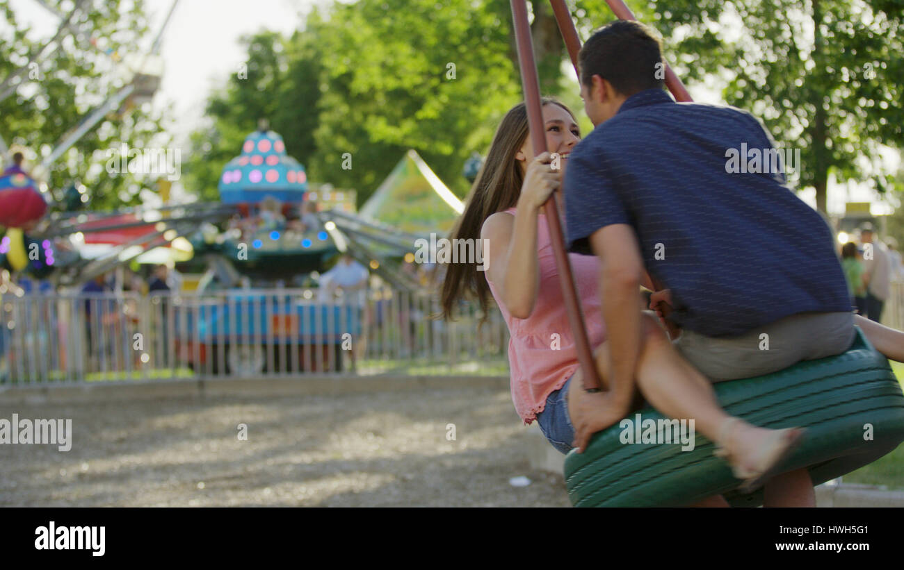 Blurred view of laughing happy boyfriend and girlfriend playing on tire swing in park Stock Photo