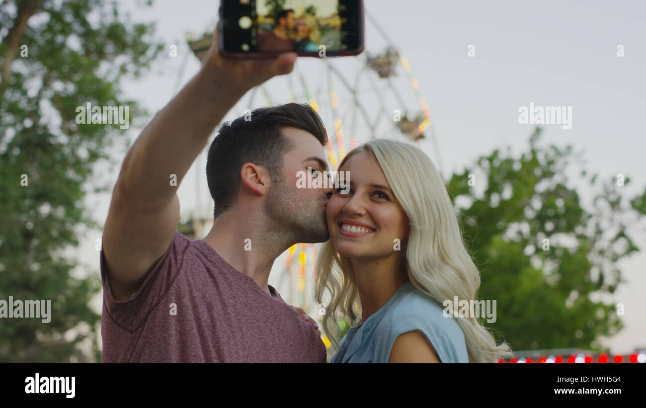 Low angle view of smiling couple kissing and taking selfie with smartphone camera outdoors Stock Photo