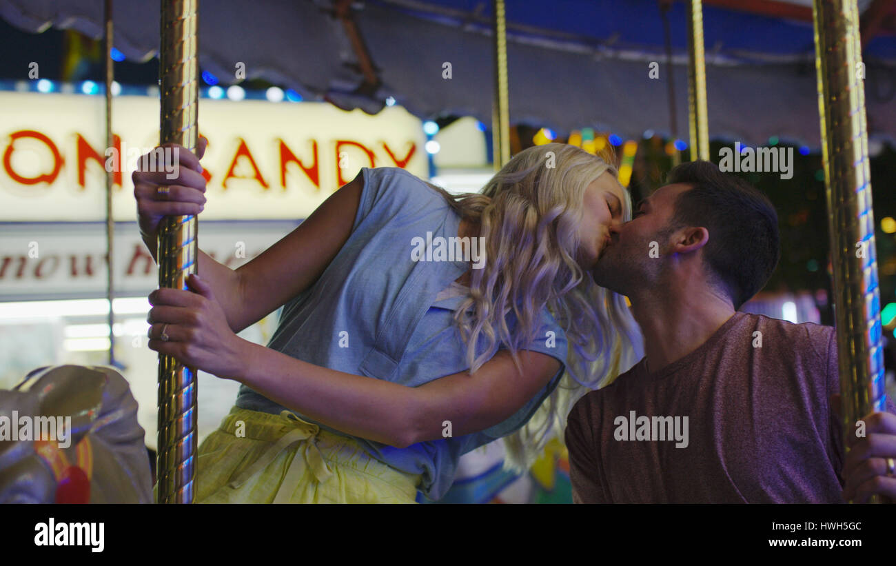 Low angle view of romantic boyfriend and girlfriend kissing on carousel at amusement park funfair Stock Photo
