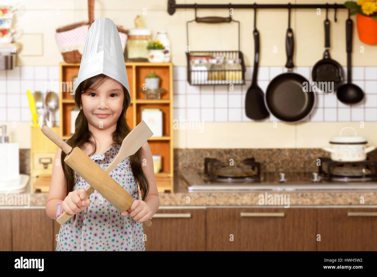 Happy asian little girl with chef hat holding cooking appliance in the kitchen room Stock Photo