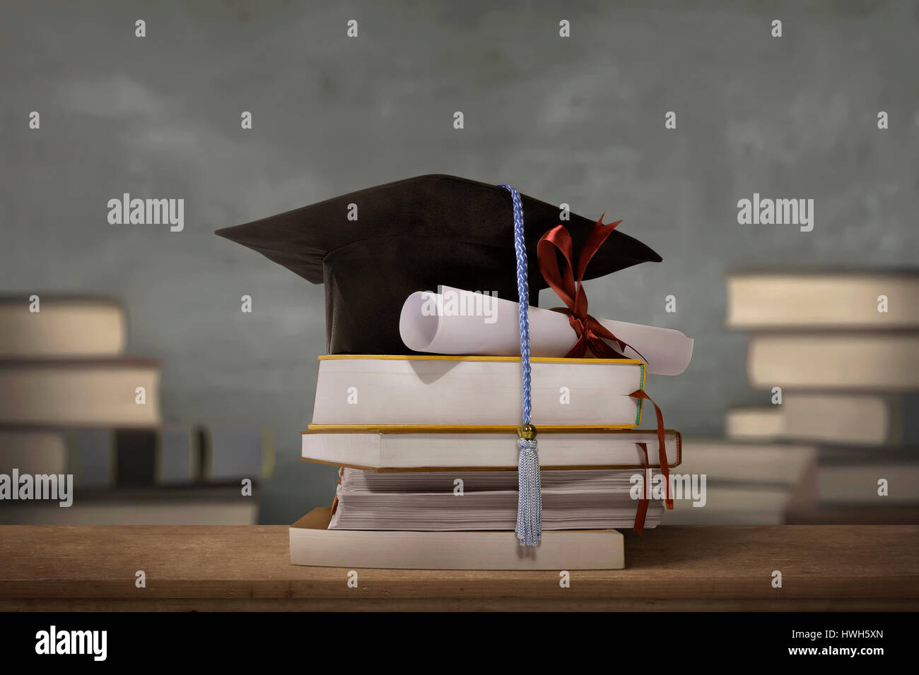 Graduation cap above stack books with degree paper on wooden table Stock Photo