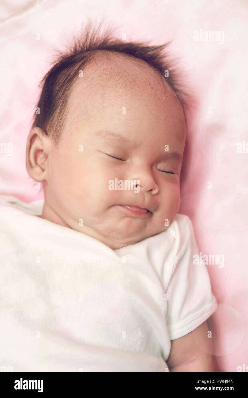 Peaceful baby lying on a bed while sleeping in a bright room over white