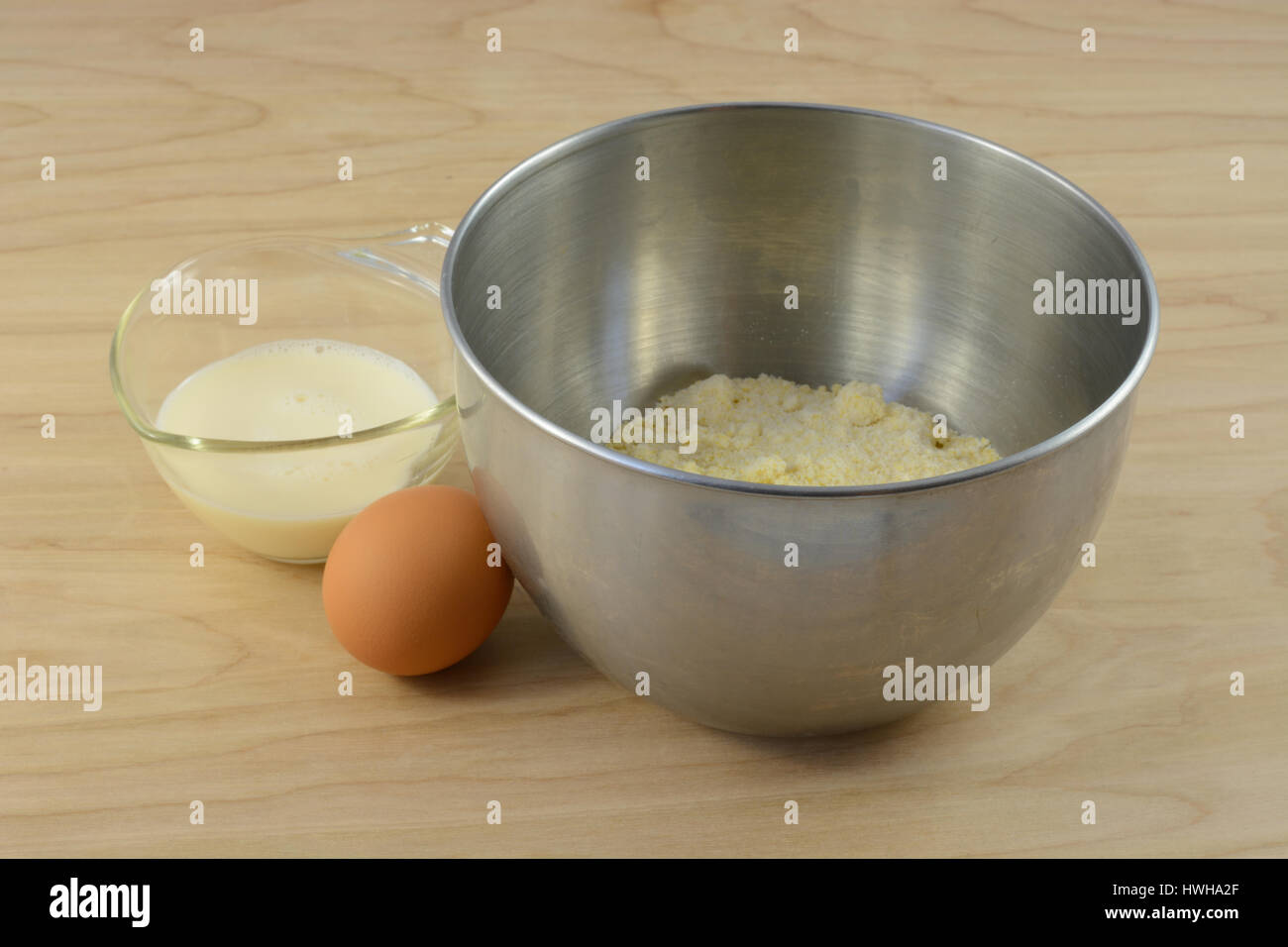Ingredients for cornbread batter with mix in mixing bowl, egg and milk in measuring cup Stock Photo