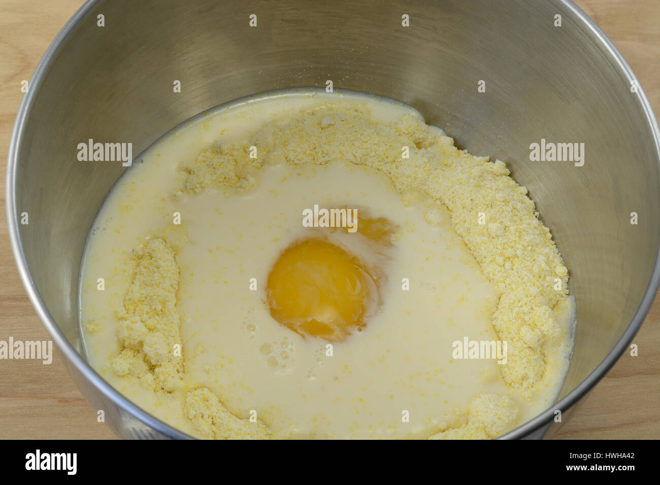 Egg and evaporated milk on top of cornbread mix in stainless steel mixing bowl Stock Photo
