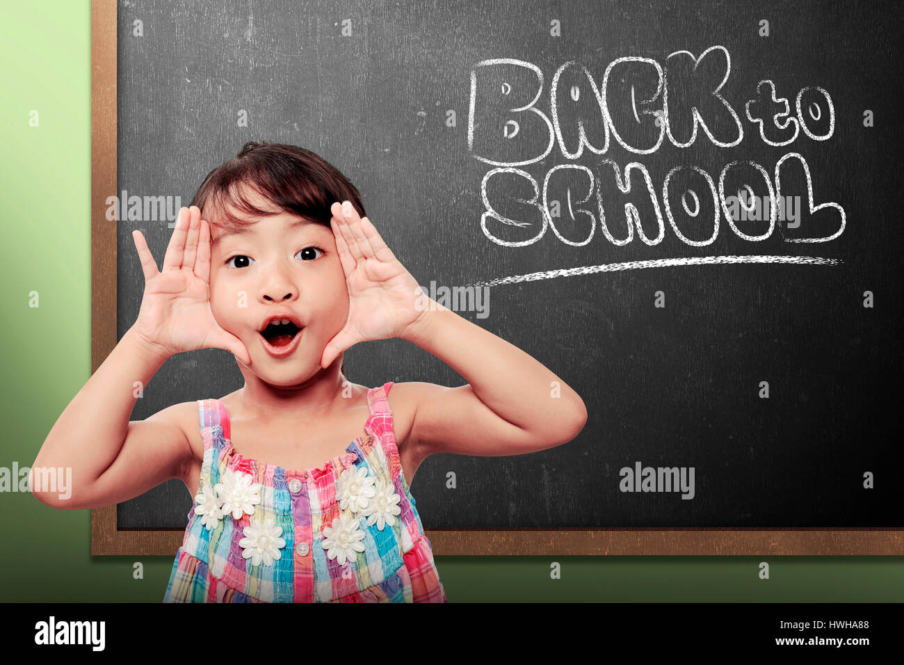 Cheerful smiling little girl on chalkboard background. Looking at camera. Back to school concept Stock Photo