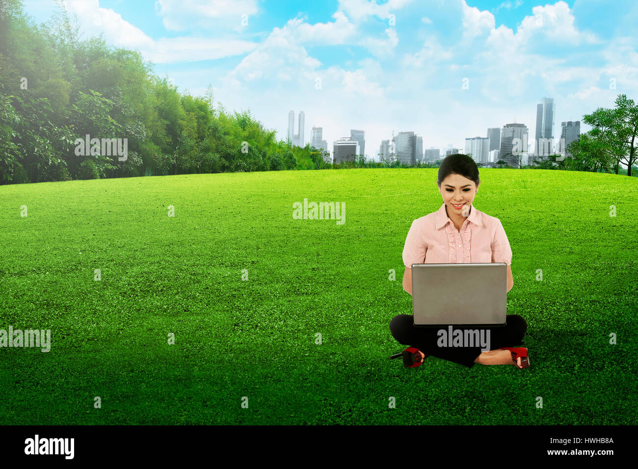 Asian woman working with laptop and sitting on the grass on city park ...