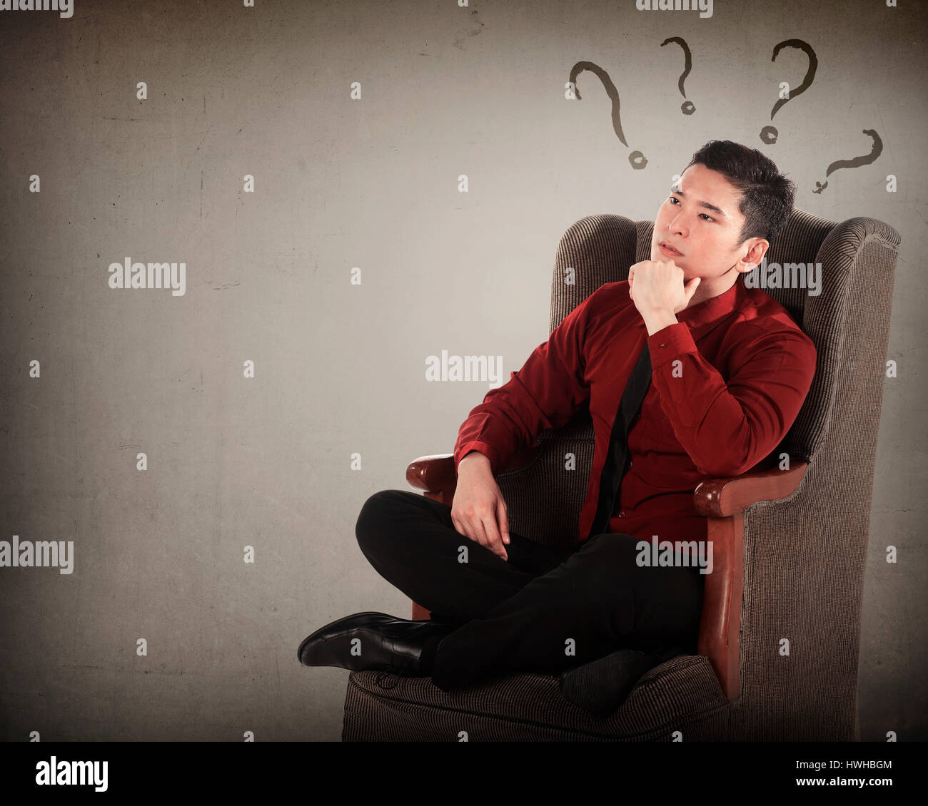 Asian business man thinking on armchair with question mark around his head Stock Photo