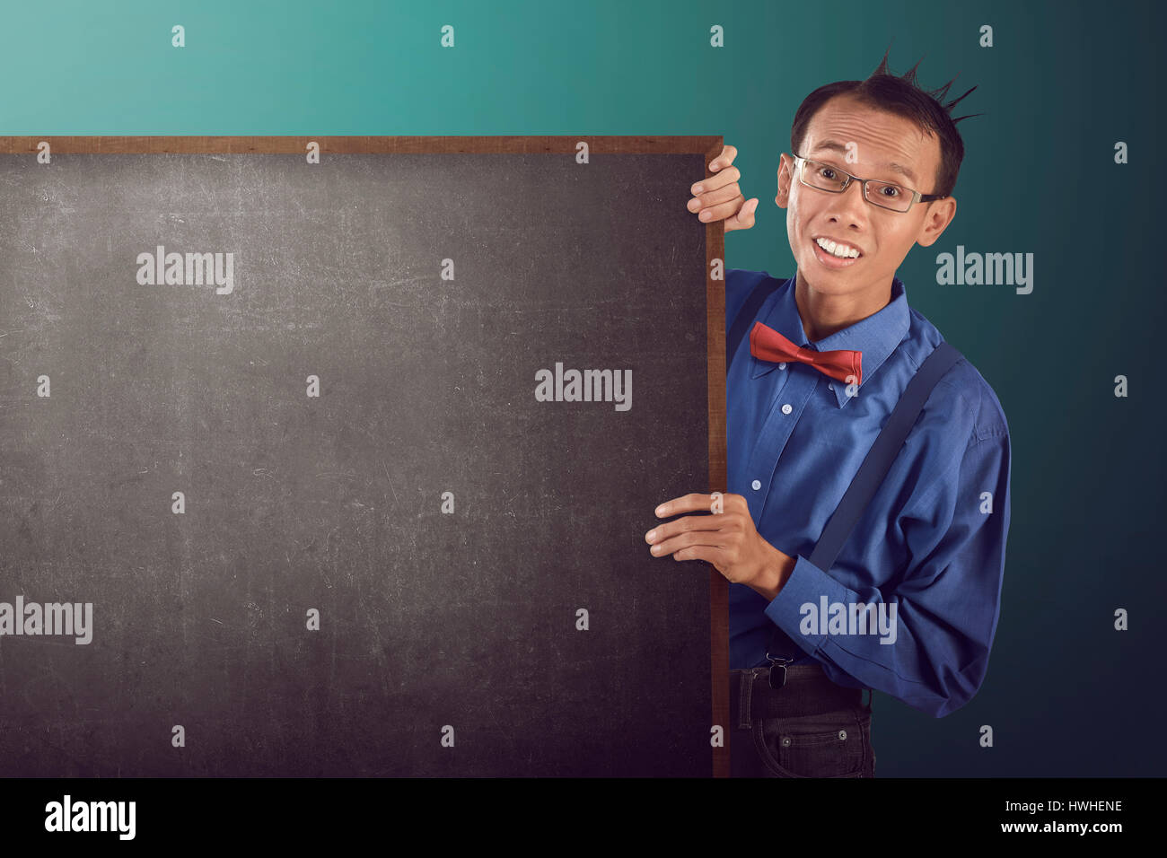 Nerdy man holding blank board, wearing blue shirt, suspender, bow tie and glasses. indoor background Stock Photo