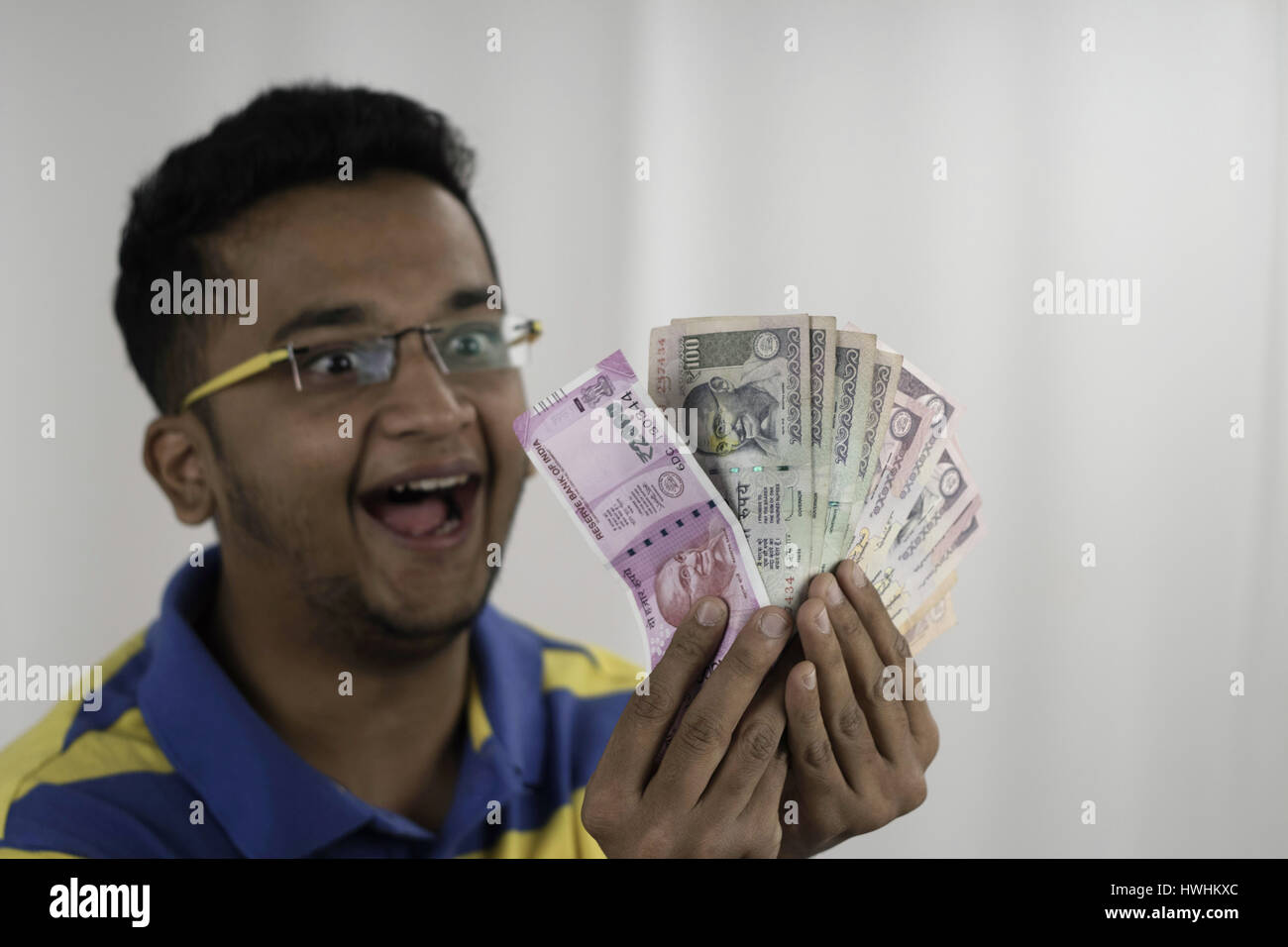 Wide eyed spectacled man going crazy with his money by fanning two thousand , hundred and fifty rupees notes. Post demonetization Stock Photo