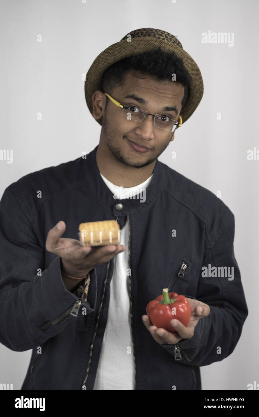 Bespectacled man with a hat and jacket challenging you to choose between unhealthy and healthy food Stock Photo