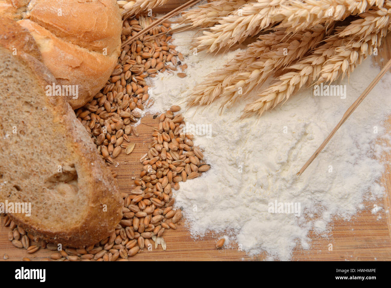 Grains, wheat ears, flour, bread and bagel on a wooden table. Concept of making food from cereals, raw material in finished product. Rustic background Stock Photo