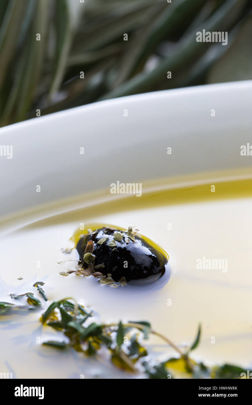 Macro shot of a black olive in white plate filled with olive oil. Stock Photo