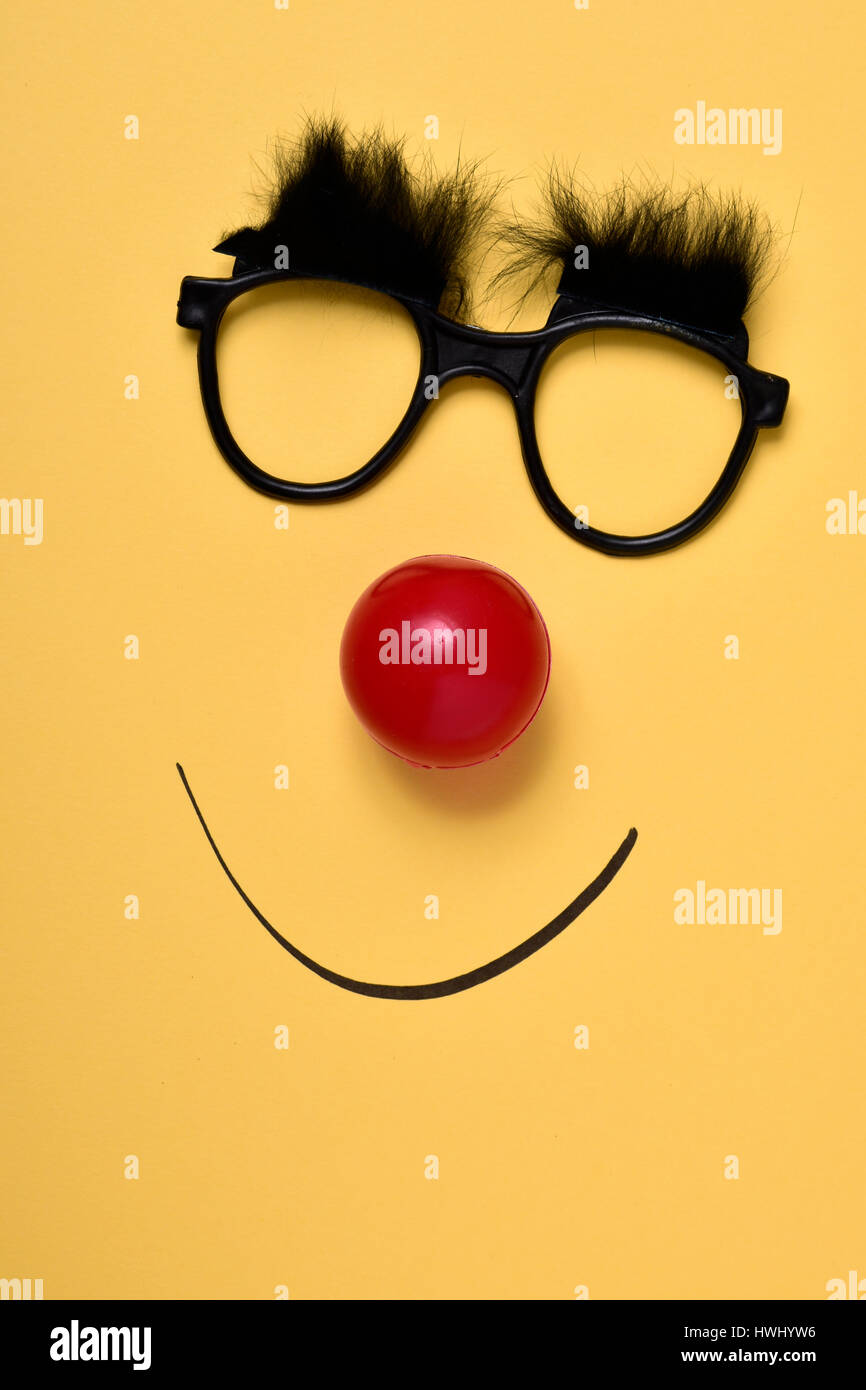 a pair of eyeglasses with bushy eyebrows, a red clown nose and a smile drawn on a yellow background Stock Photo