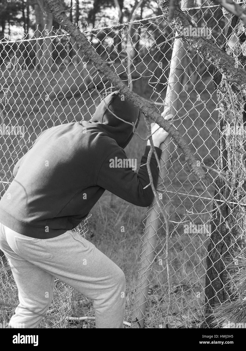 Person crawling through a fence opening with hand clinging to a steel wire , black and white, Australia 2016 Stock Photo