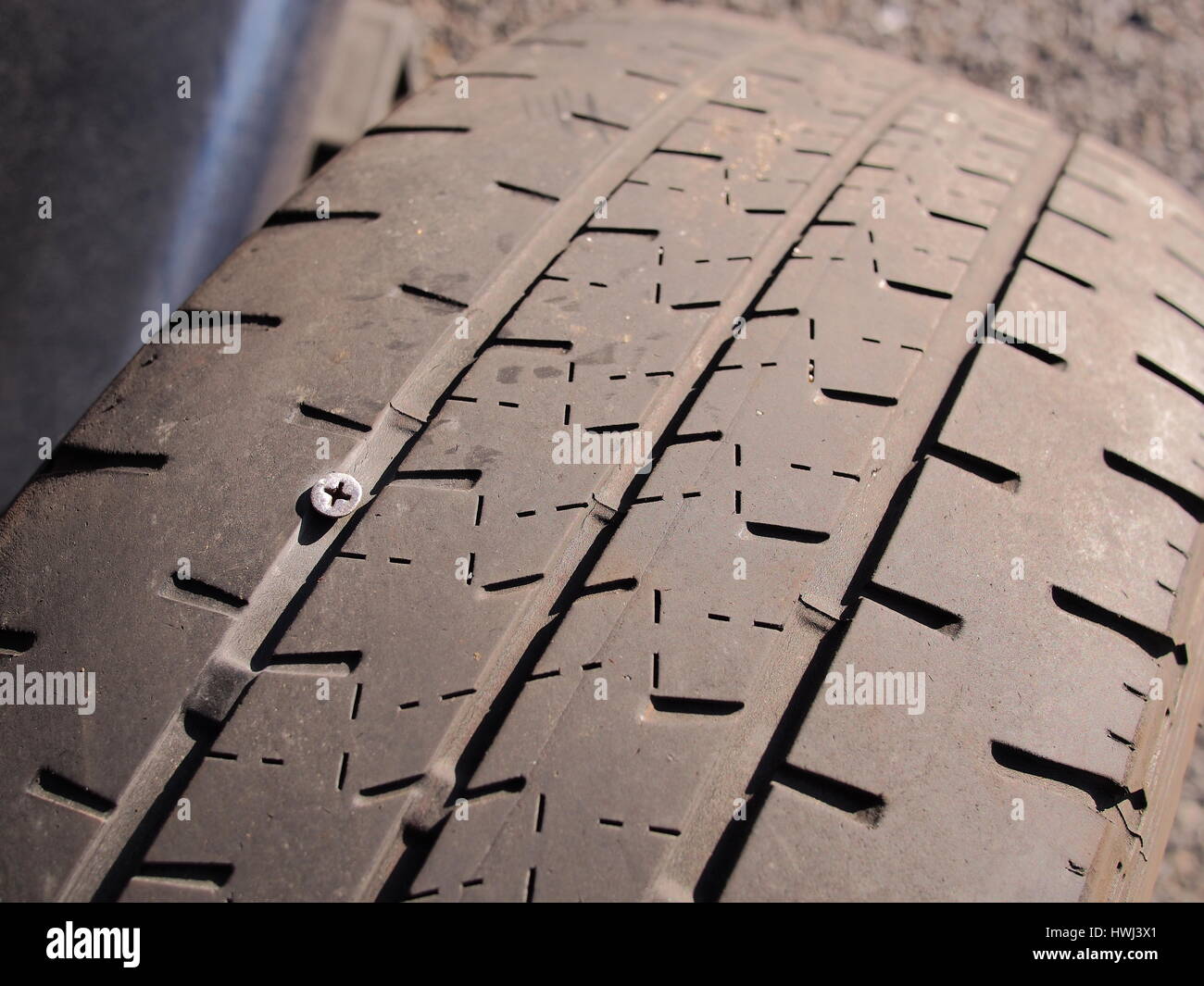 Flat car tire with a silver Philips head screw pierced through the ...