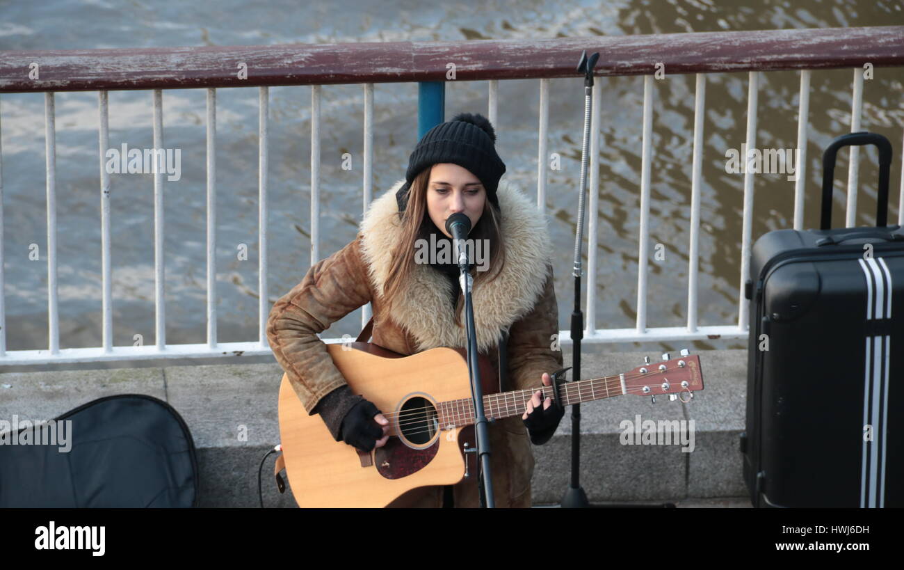 a beautiful young female singer and guitarist musician playing on the south bank of the river thames with parliament in the back ground Stock Photo