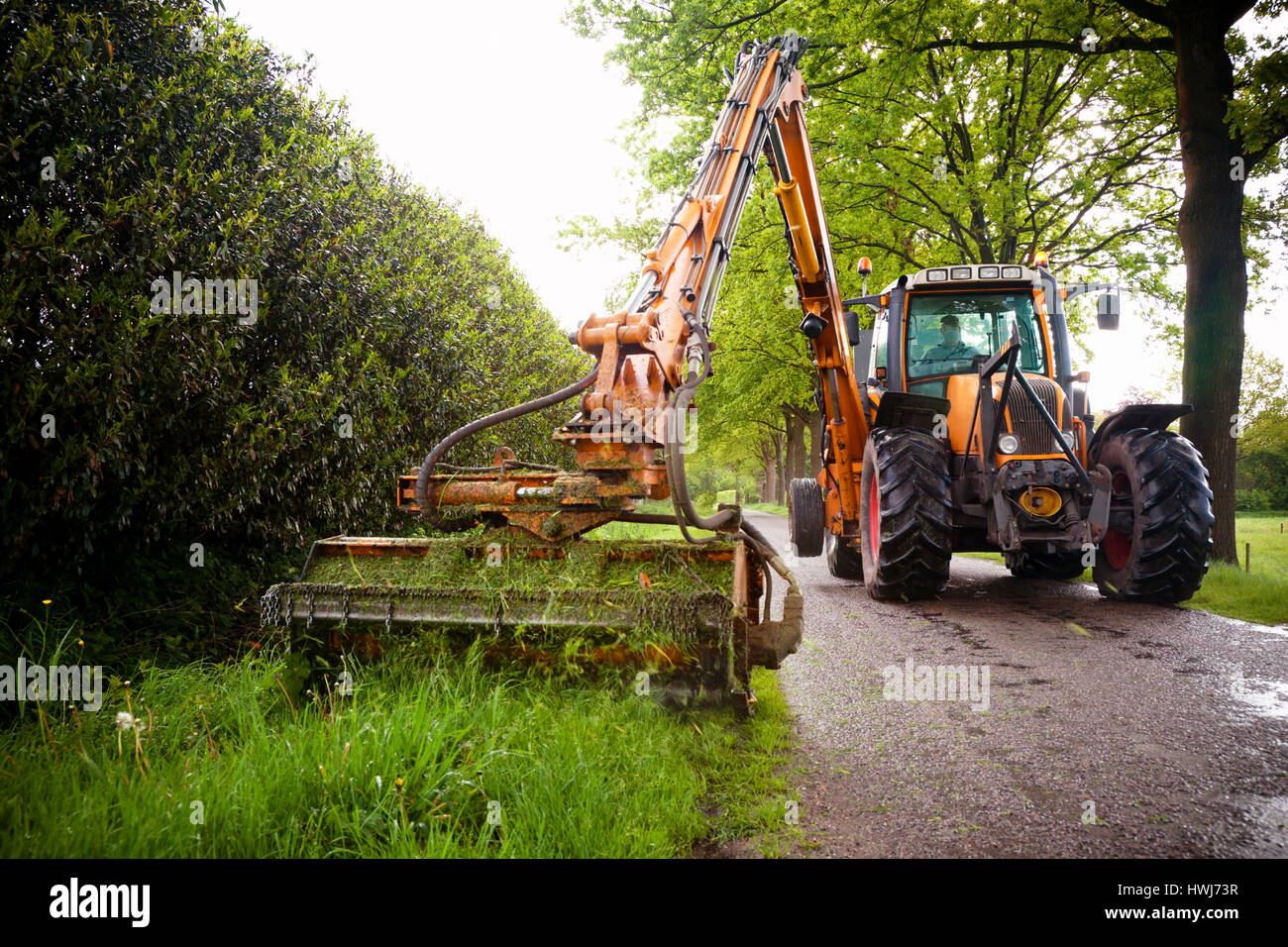 mowing grass shoulder along road in public space  with big orange tractor mower Stock Photo