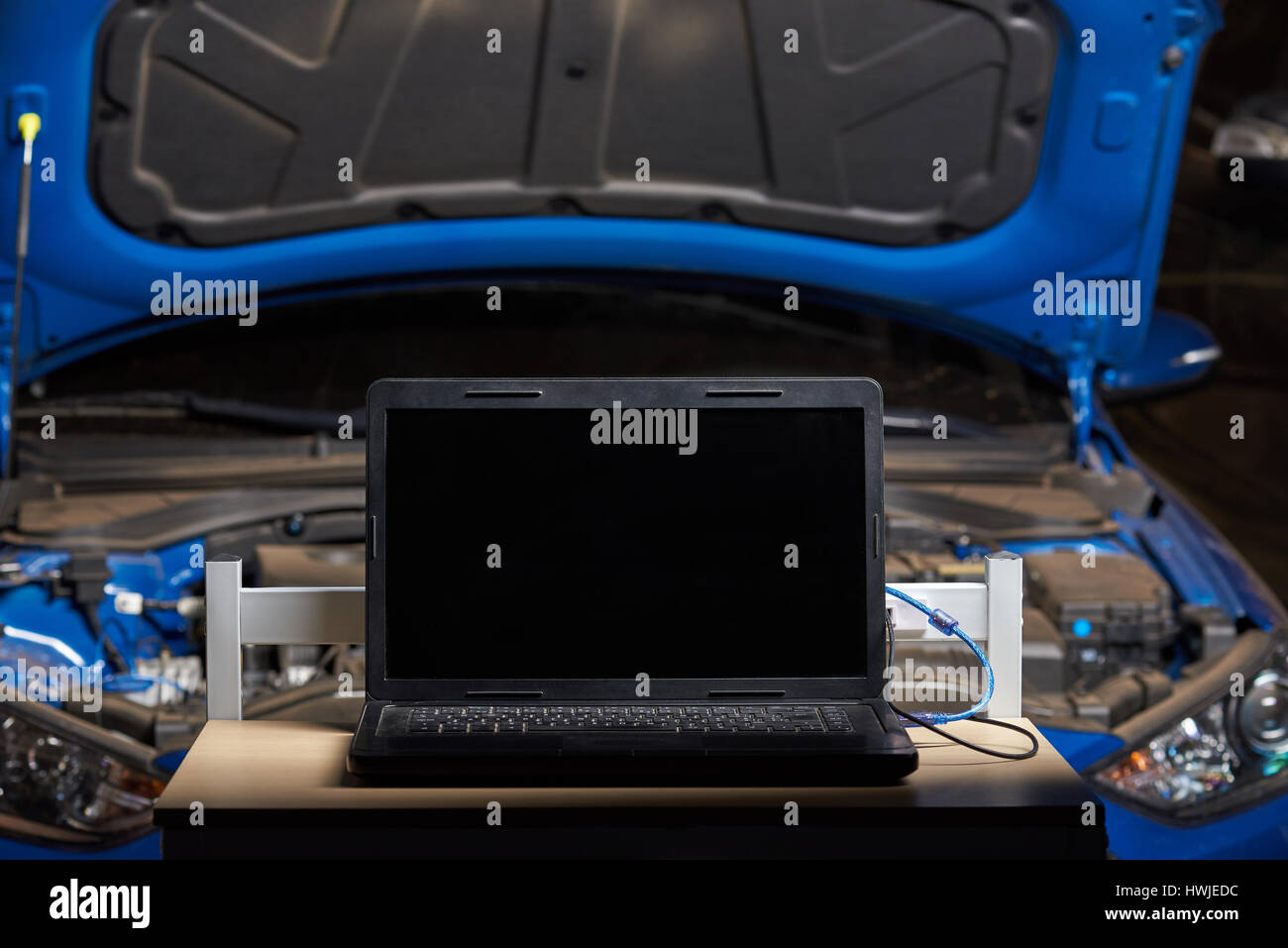 Laptop for computer car diagnostic on clean table station blurred blue vehicle open hood background Stock Photo