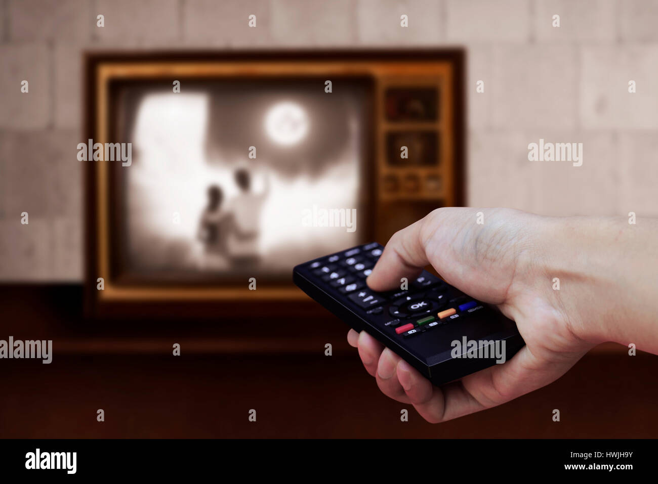Man hand holding TV remote control with a television in the background Stock Photo