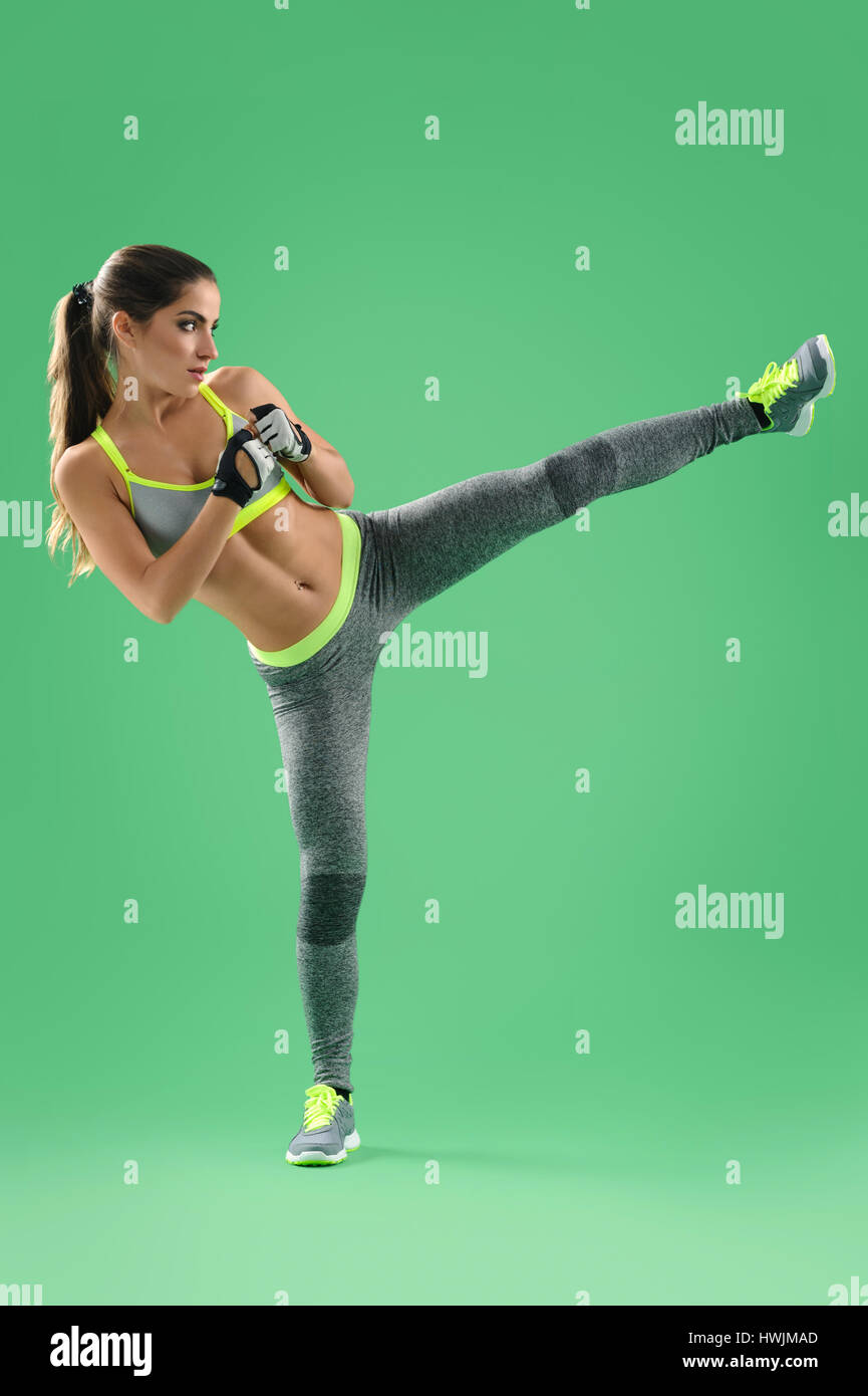 Athletic woman training her high kick in studio on green backgro Stock