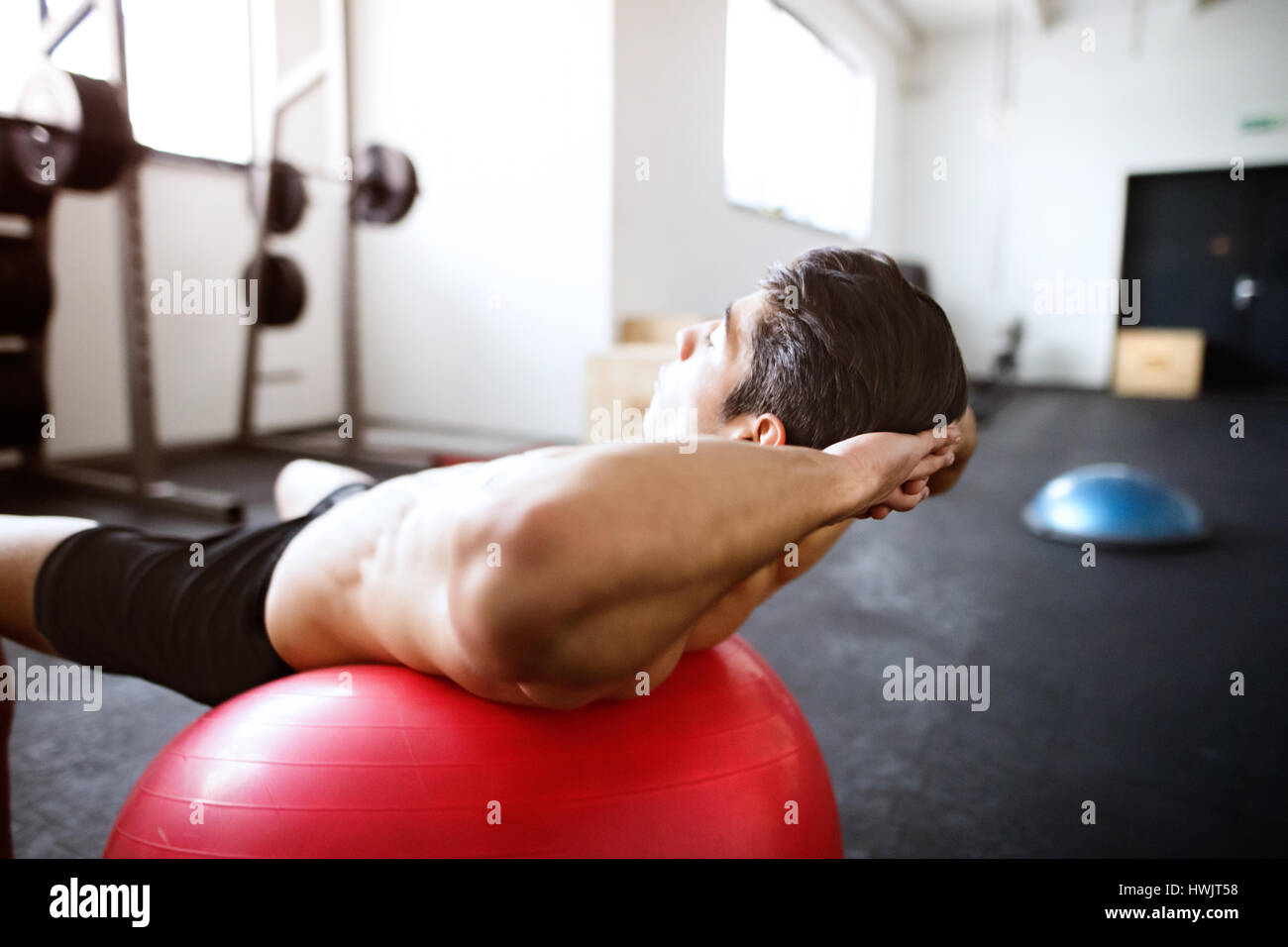 Fit hispanic man at abdominal crunch muscles exercises on red fitness ball during training in