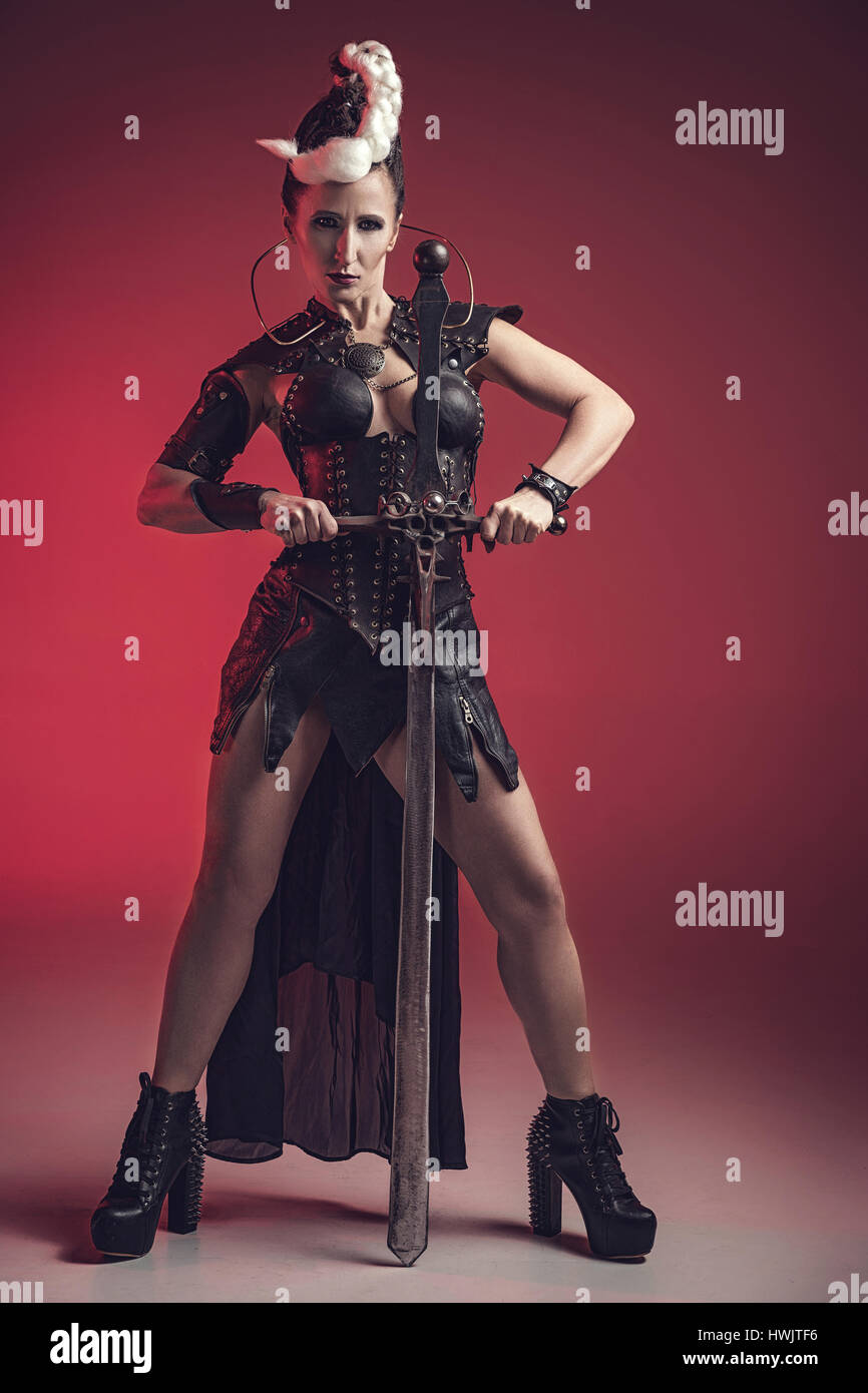 Beautiful warrior woman. Fantasy fighter. Princess or queen in leather corset ready for war. Red light and white weapon. Stock Photo