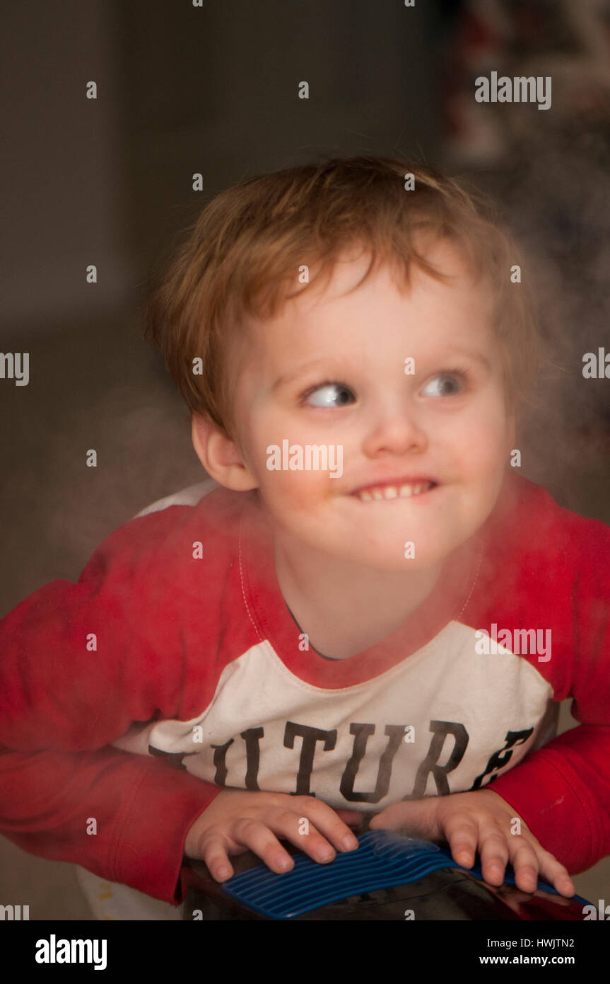 2-3 YEAR OLD CAUCASIAN MALE WITH SNEAKY FACE IN HUMIDIFIER STEAM. Stock Photo
