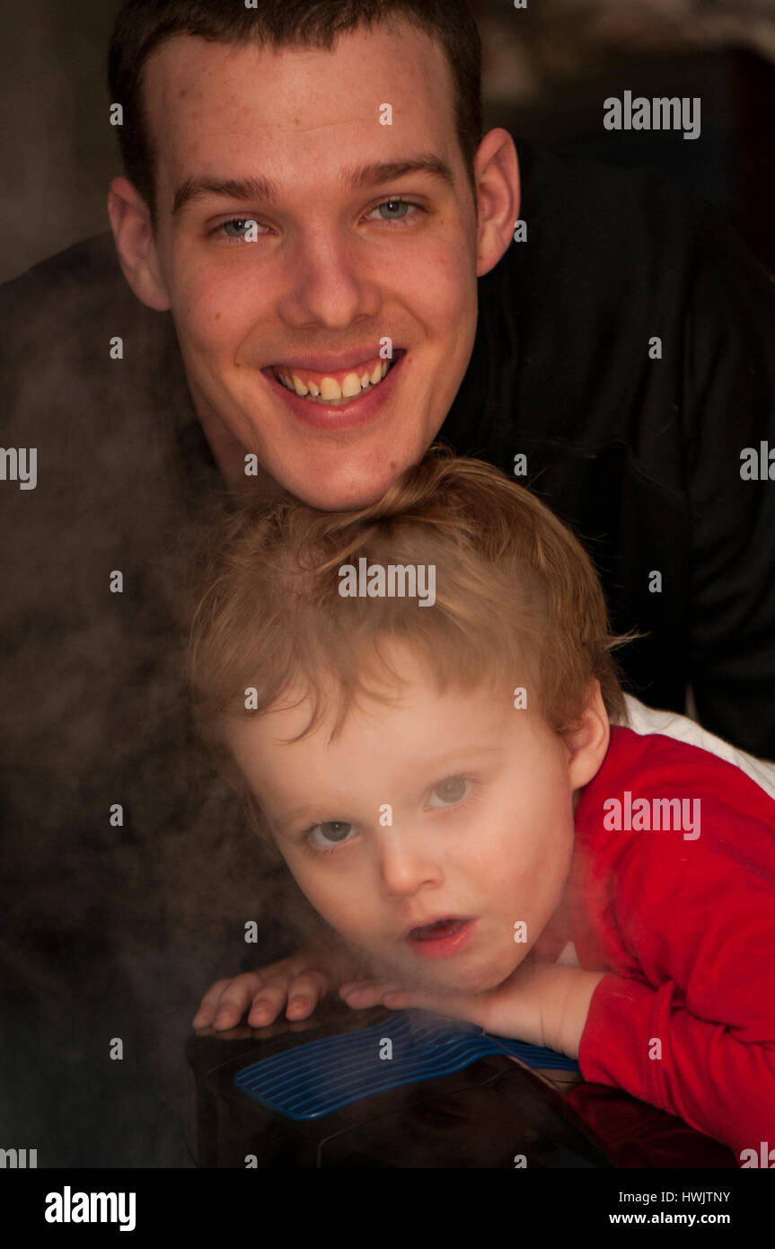 25-30 YEAR OLD FATHER WITH 2-3 YEAR OLD CAUCASIAN SON IN STEAM FROM A HUMIDIFIER. Stock Photo