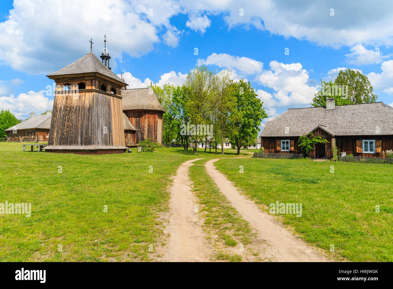 Rural road in Tokarnia village with old wooden church on sunny spring day, Poland Stock Photo