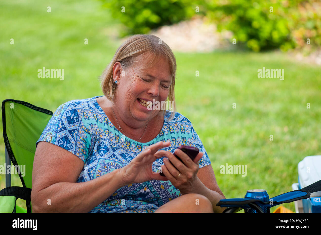 50-55 YEAR OLD CAUCASIAN WOMAN LAUGHING WHILE TEXTING ON HER IPHONE. Stock Photo