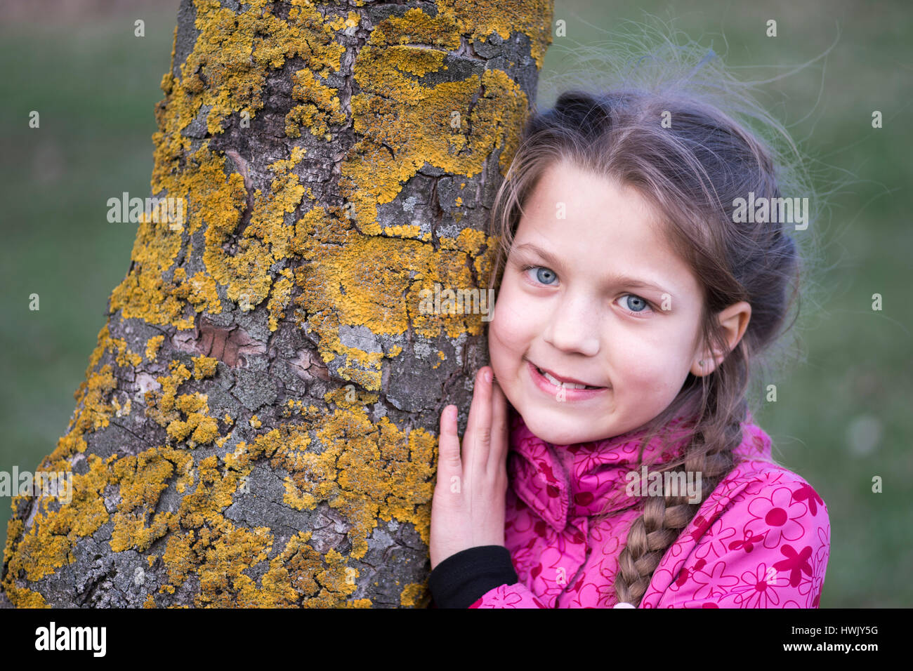 smiling child girl lean on chestnut tree stem by springtime Stock Photo