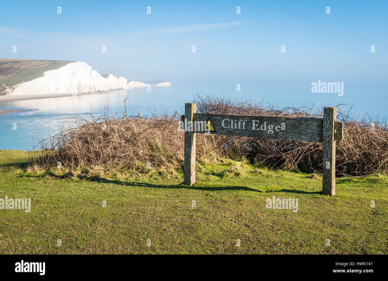 Sign warning of cliff edge at Seaford Head Nature Reserve, East Sussex, with the Seven Sisters cliffs in the background Stock Photo