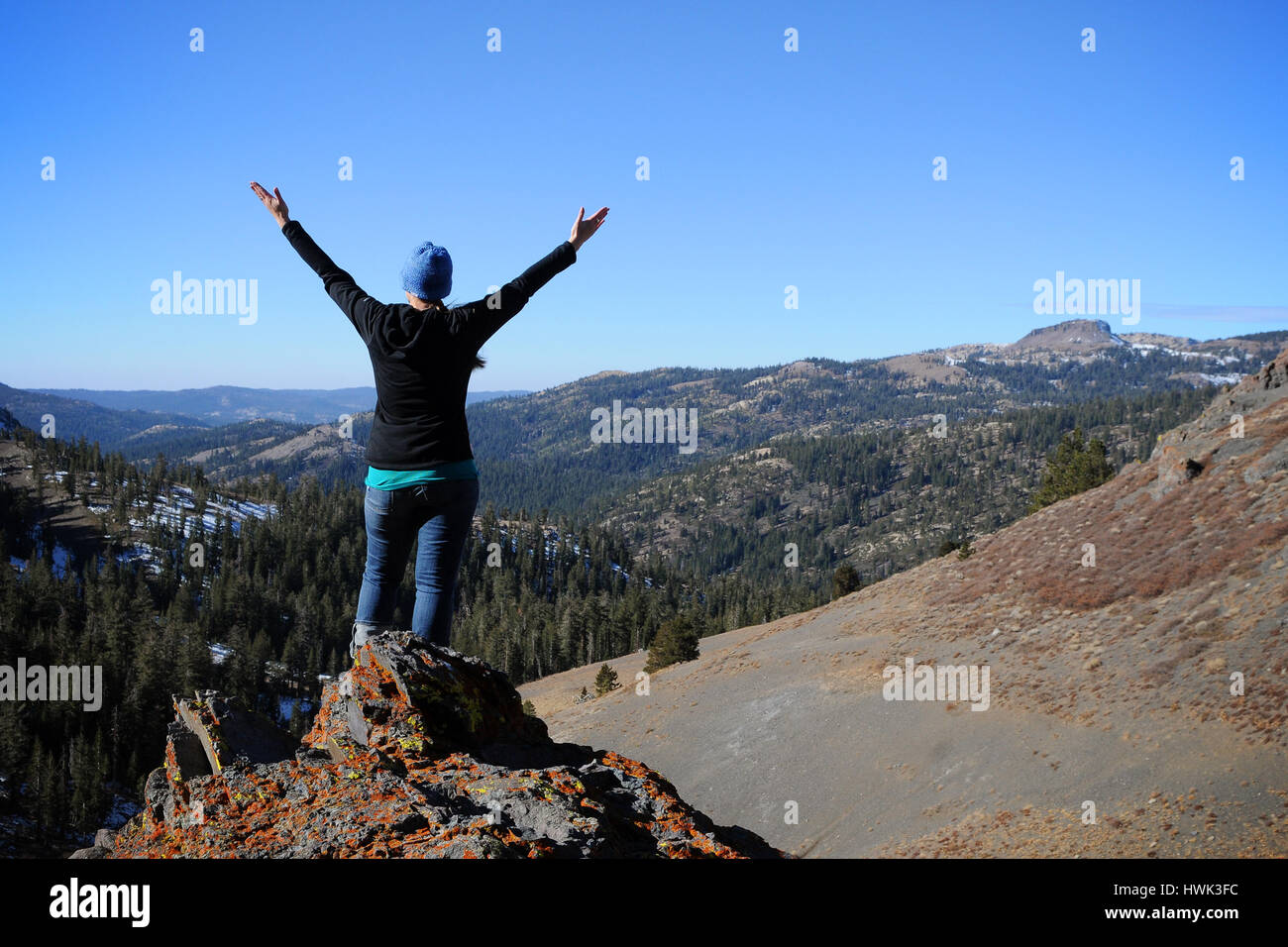 A woman with her back to the camera, stands on a rock and holds her ...