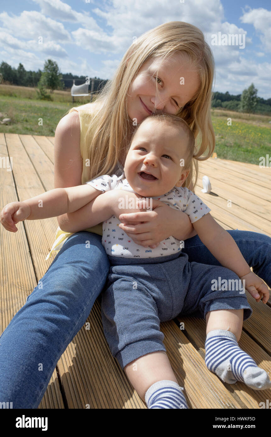 Adoring sister holding happy baby brother on the deck. Polish children age 8 and 7 months. Zawady Central Poland Europe Stock Photo