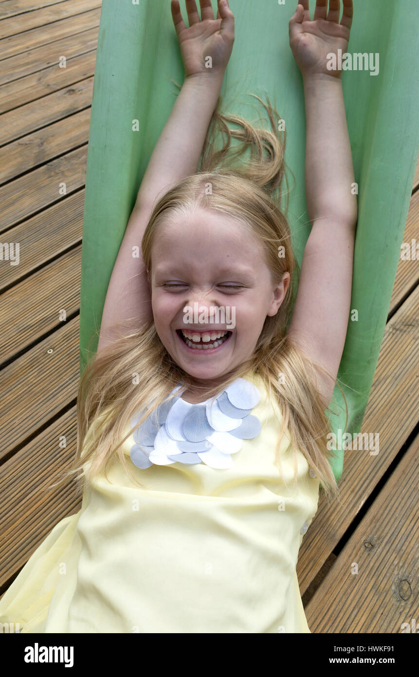 Exuberant young girl laughing at the bottom of her slide on the deck. Polish child age 8. Zawady Central Poland Europe Stock Photo