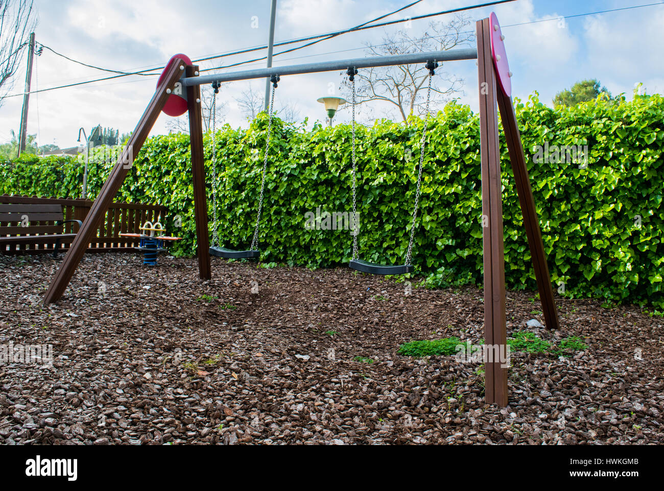 Empty swings with chains swaying at playground for child, ivy on the background Stock Photo