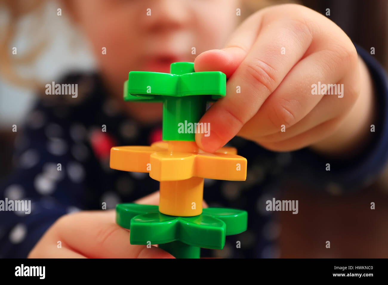 Kid building tower with constructor close-up. Closeup of constructor in children hands. Toy tower on defocused child happy face background. Stock Photo